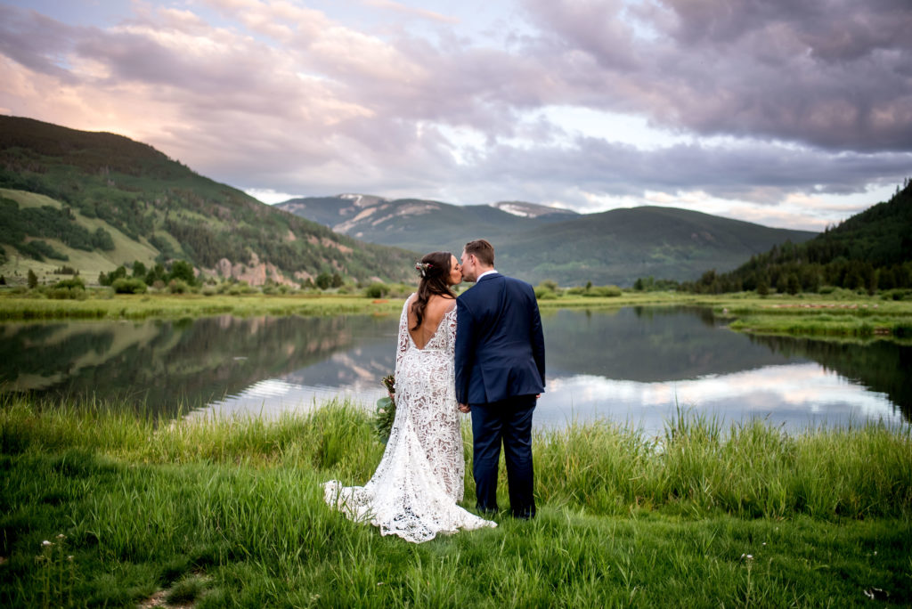 Bride and groom kissing at sunset by a lake at Vail wedding venue Camp Hale in Vail, Colorado