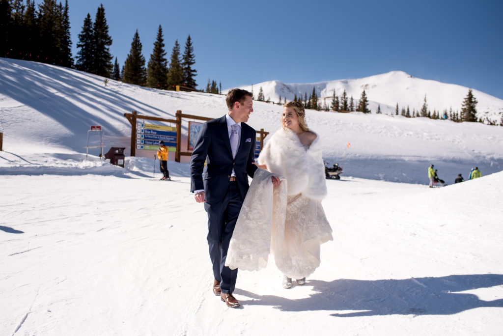 Couple walking by skiers and snowboarders at the top of Breckenridge mountain during their winter ski resort elopement in Colorado