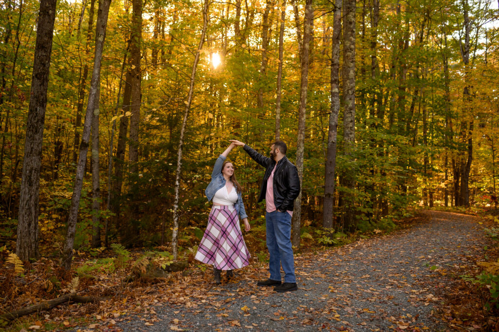 Couple in a dancing spin with sun shining through foliage in the woods of NH.