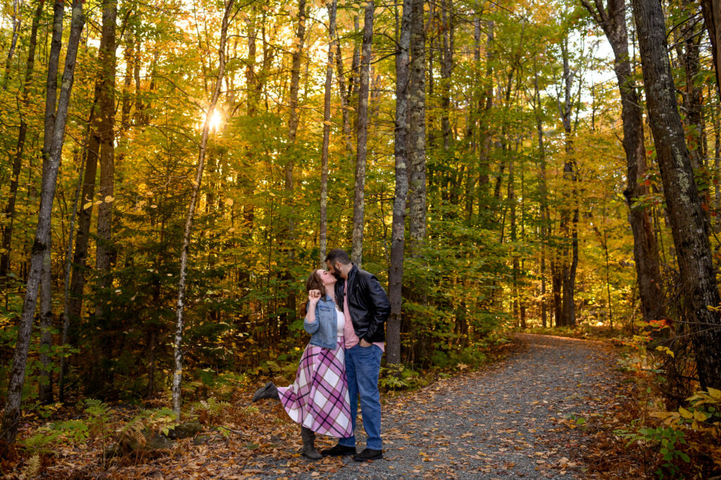 Engaged couple kissing on wooded path