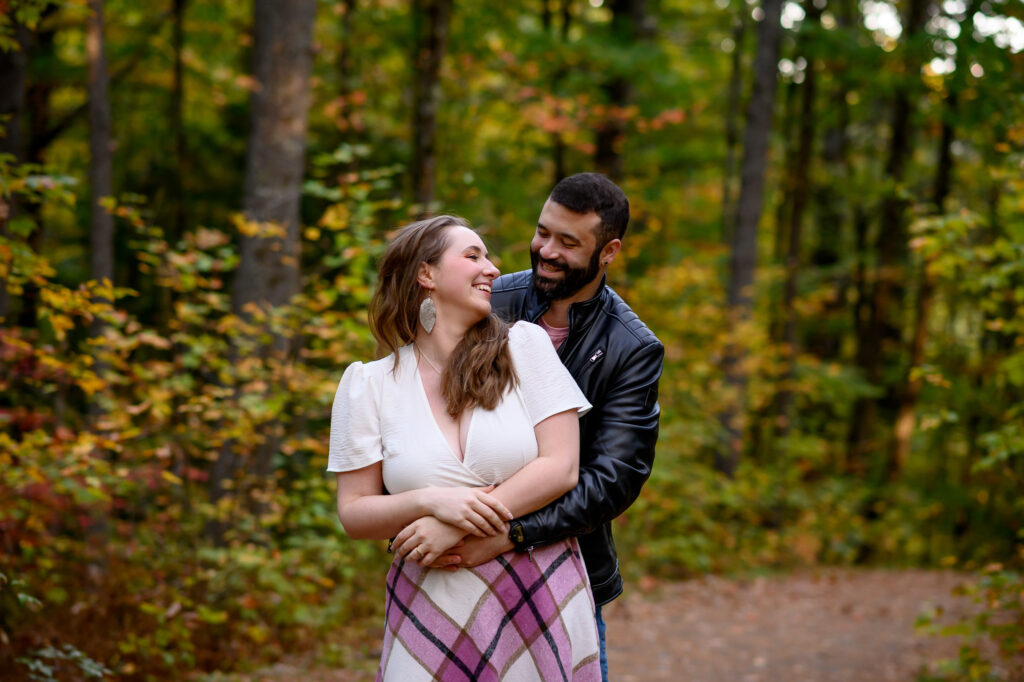 Closeup of couple looking at eachother laughing in a new england forest surrounded by foliage