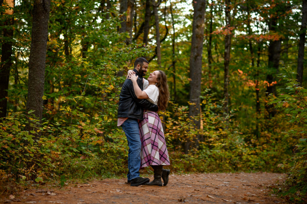 Couple mid laugh while holding each other on a walking trail in NH