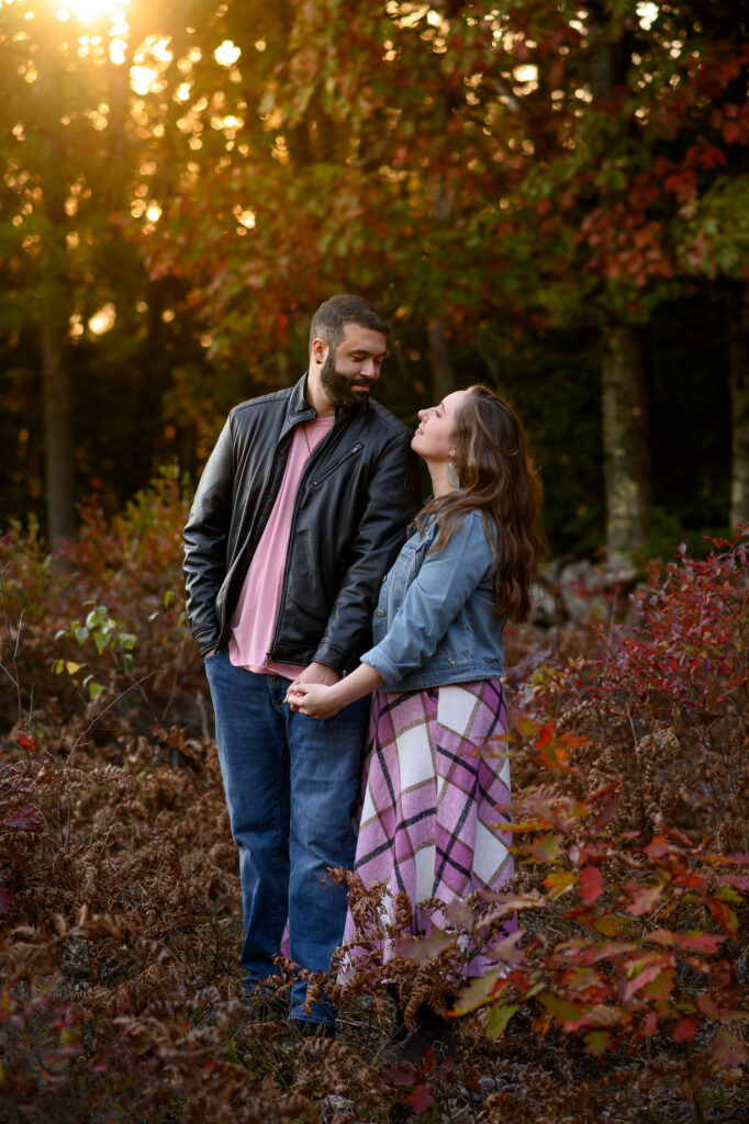 Couple looking at eachother hand in hand surrounded by foliage reds during golden hour