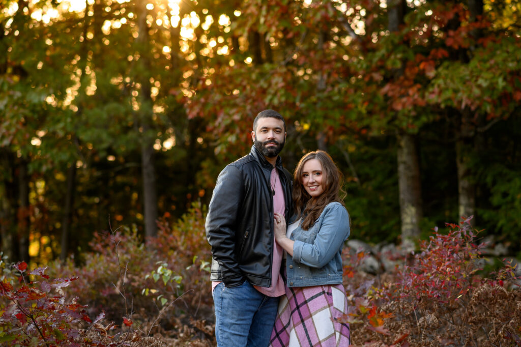 Couple smiling at camera surrounded by warm reds of peak fall golden light