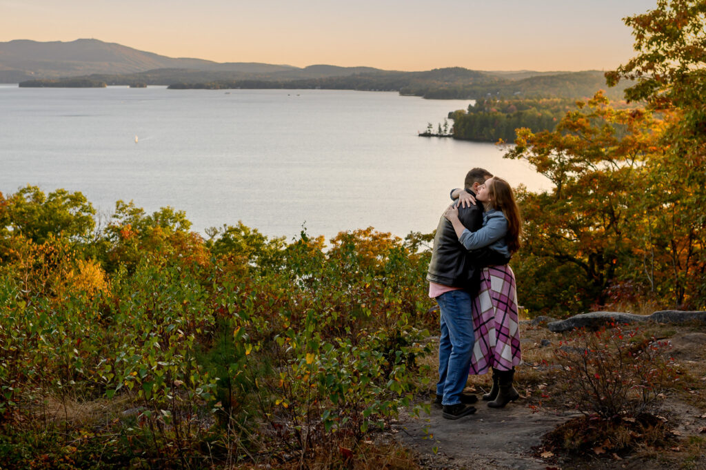 Couple embracing with Lake Sunapee and fall foliage behind them