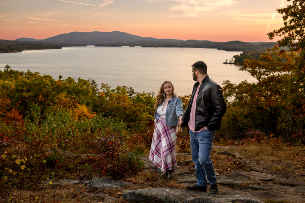 couple holding hands and looking towards each other as they guide one another up a hill overlooking lake sunapee